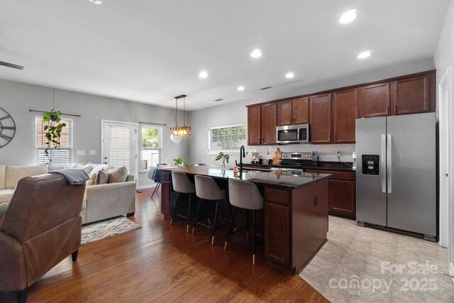 kitchen with stainless steel appliances, open floor plan, dark countertops, a kitchen breakfast bar, and a kitchen island with sink