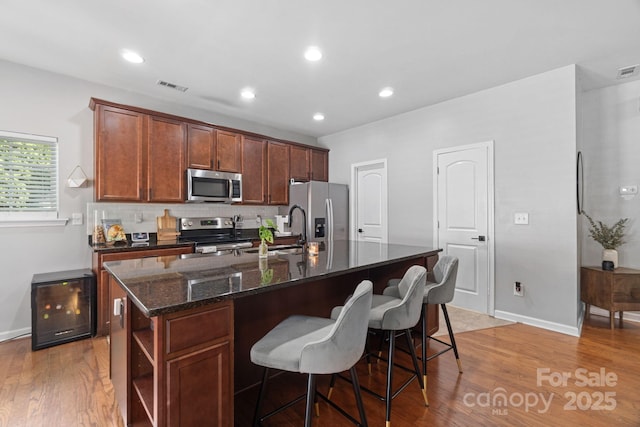 kitchen featuring stainless steel appliances, a sink, a center island with sink, light wood-style flooring, and recessed lighting