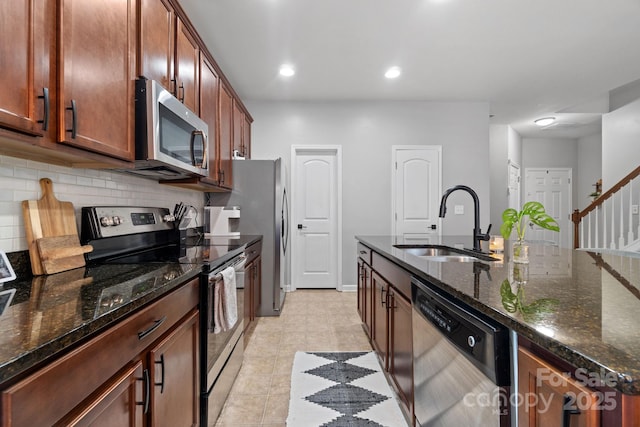 kitchen featuring stainless steel appliances, a sink, tasteful backsplash, dark stone countertops, and a center island with sink