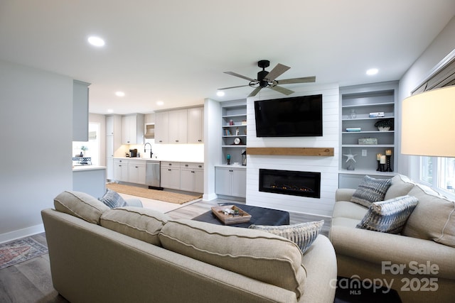 living room featuring wood finished floors, a ceiling fan, a fireplace, baseboards, and recessed lighting