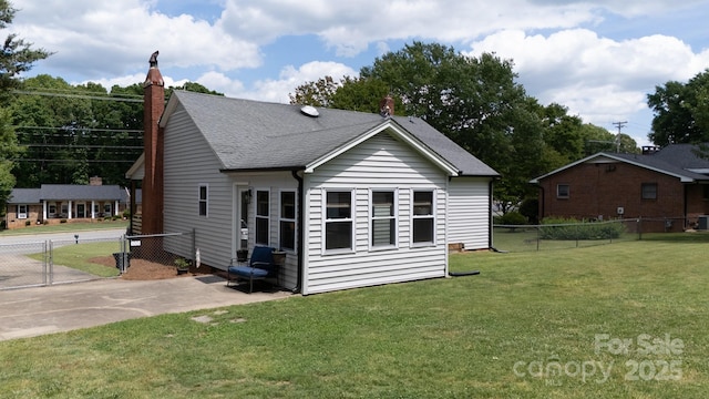 rear view of property featuring a yard, roof with shingles, a chimney, and fence