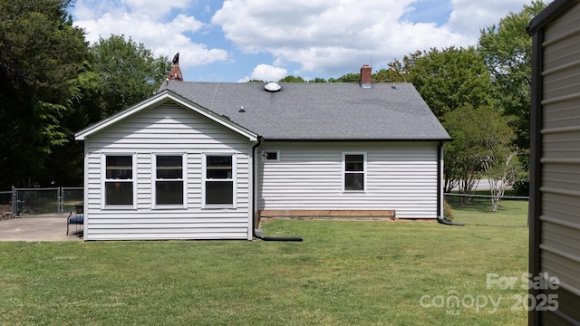 back of house with roof with shingles, fence, a chimney, and a lawn