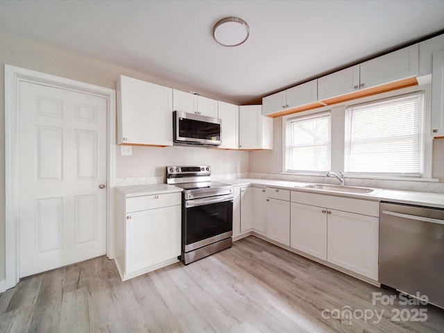 kitchen with appliances with stainless steel finishes, a sink, light countertops, and white cabinetry