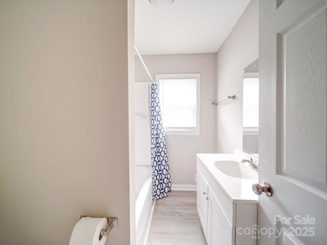 bathroom featuring vanity, wood finished floors, shower / bath combo with shower curtain, baseboards, and toilet