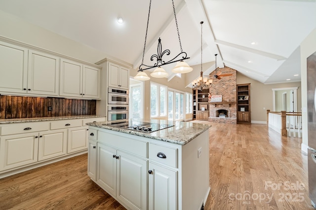 221 Stillwater Rd, Troutman, NC 28166 - kitchen featuring black electric stovetop, a kitchen island, stainless steel double oven, light wood finished floors, and a brick fireplace