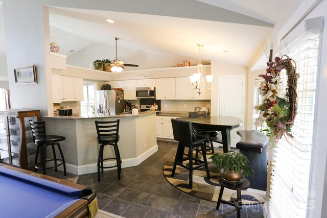 kitchen featuring appliances with stainless steel finishes, lofted ceiling, a peninsula, white cabinetry, and a breakfast bar area