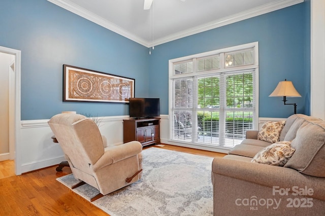 living room featuring crown molding, wood finished floors, a wainscoted wall, and ceiling fan
