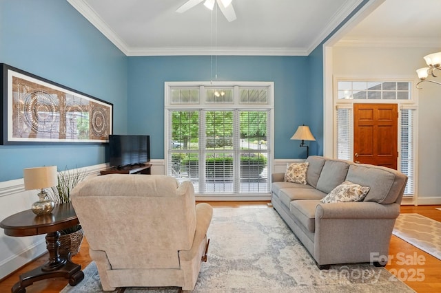 living area with crown molding, ceiling fan, wood finished floors, and wainscoting