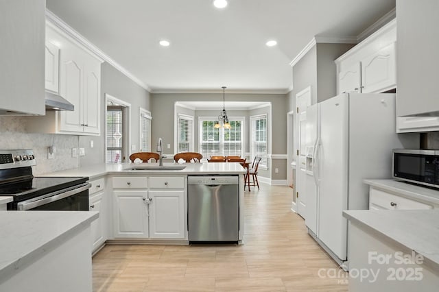 kitchen featuring stainless steel appliances, a sink, ornamental molding, white cabinets, and a peninsula