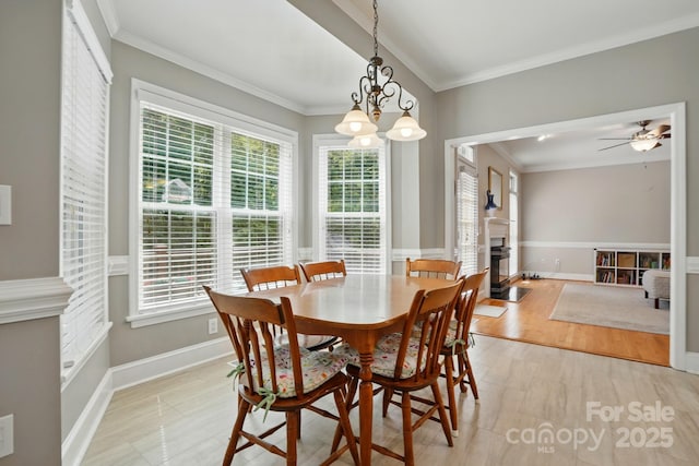 dining room featuring a fireplace with flush hearth, crown molding, plenty of natural light, a chandelier, and baseboards