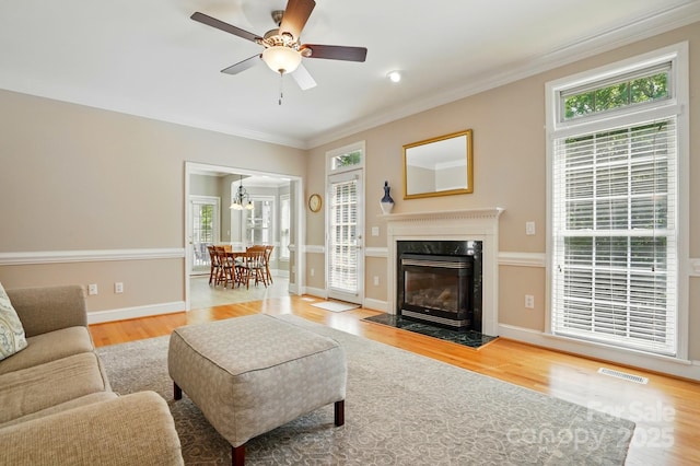 living room featuring light wood finished floors, crown molding, ceiling fan, a fireplace, and baseboards