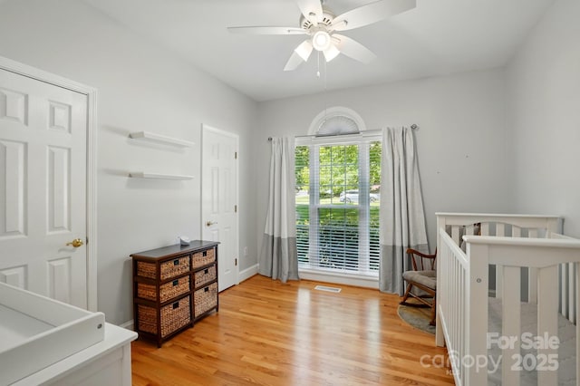 bedroom featuring light wood-style floors, a crib, ceiling fan, and baseboards