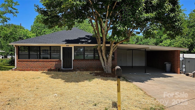 view of front of property featuring brick siding, concrete driveway, a carport, and a shingled roof
