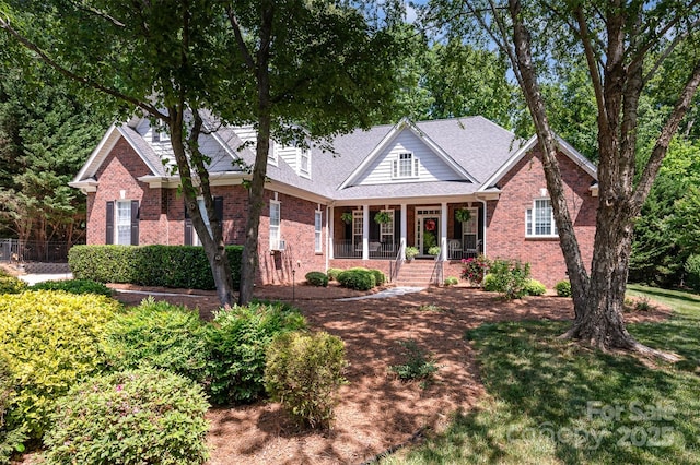view of front of house featuring brick siding, covered porch, and fence