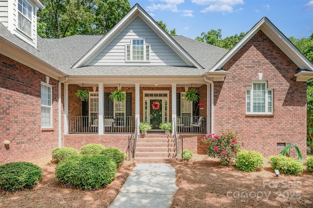view of front of house with a porch, a shingled roof, and brick siding