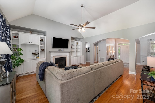 living area with arched walkways, lofted ceiling, a ceiling fan, built in features, and a fireplace