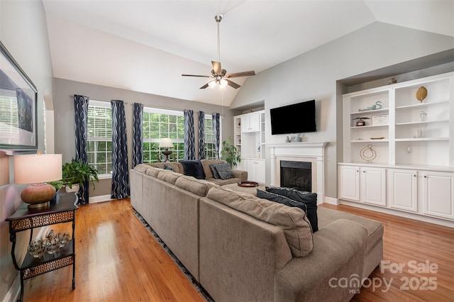living room with lofted ceiling, a fireplace, light wood-type flooring, a ceiling fan, and baseboards
