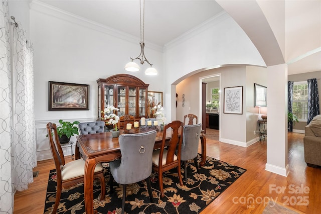 dining space with arched walkways, light wood-style floors, ornamental molding, baseboards, and a towering ceiling