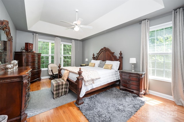 bedroom featuring a raised ceiling, baseboards, light wood finished floors, and ceiling fan