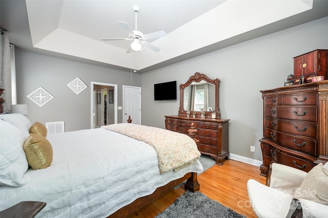 bedroom featuring light wood-style flooring, a raised ceiling, baseboards, and ceiling fan