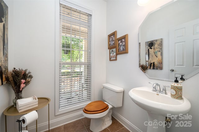 half bathroom featuring baseboards, tile patterned floors, toilet, and a sink