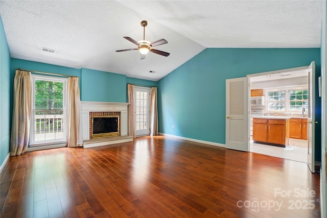 unfurnished living room with ceiling fan, wood finished floors, vaulted ceiling, healthy amount of natural light, and a textured ceiling
