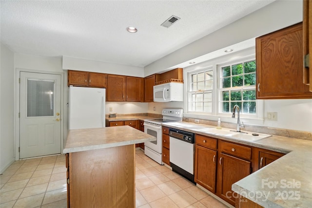kitchen featuring white appliances, a sink, light countertops, a center island, and light tile patterned floors