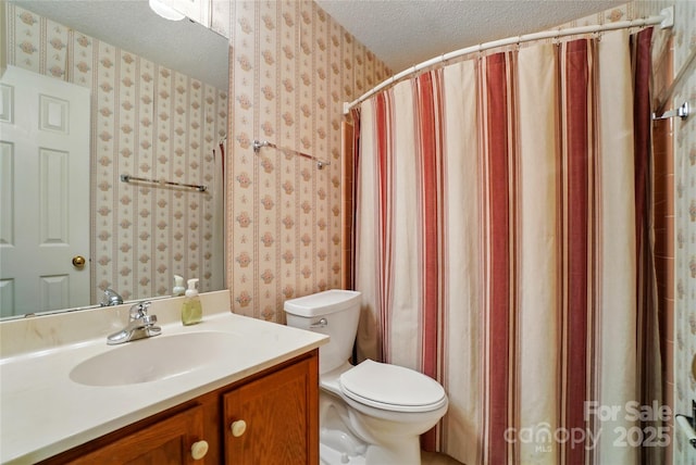 bathroom featuring a textured ceiling, wallpapered walls, toilet, and vanity