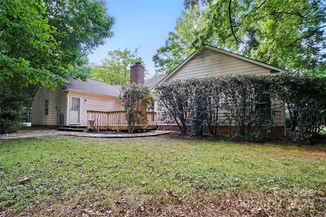 rear view of property featuring a deck, a chimney, and a lawn