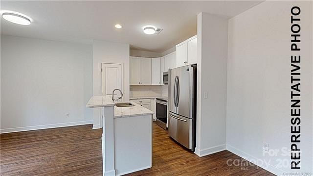 kitchen featuring stainless steel appliances, a sink, dark wood finished floors, an island with sink, and baseboards