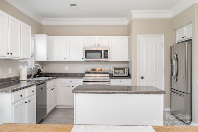 kitchen featuring stainless steel appliances, a sink, crown molding, dark countertops, and white cabinets