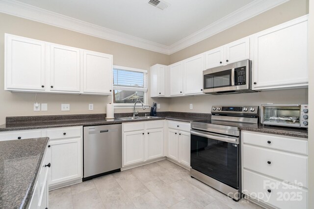 kitchen featuring stainless steel appliances, a sink, crown molding, white cabinets, and dark stone counters