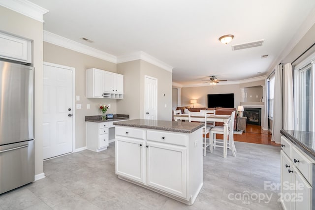 kitchen with freestanding refrigerator, a ceiling fan, crown molding, a fireplace, and white cabinets