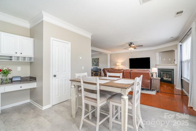 dining room featuring a ceiling fan, crown molding, a glass covered fireplace, and baseboards