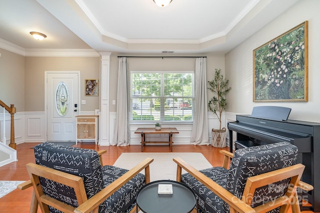sitting room featuring wood finished floors, ornamental molding, a wainscoted wall, a raised ceiling, and a decorative wall