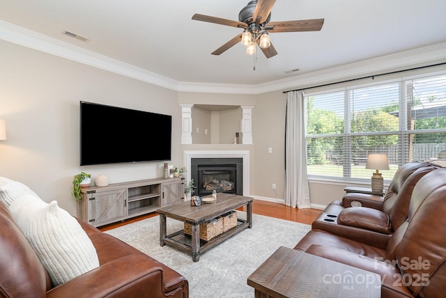 living room with ceiling fan, ornamental molding, wood finished floors, baseboards, and a glass covered fireplace
