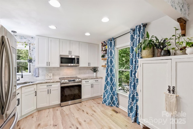 27037 Tidal Way, Tega Cay, SC 29708 - kitchen with stainless steel appliances, a sink, white cabinets, light wood-style flooring, and tasteful backsplash