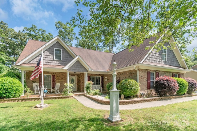 craftsman-style house with brick siding, a front lawn, a shingled roof, and a porch