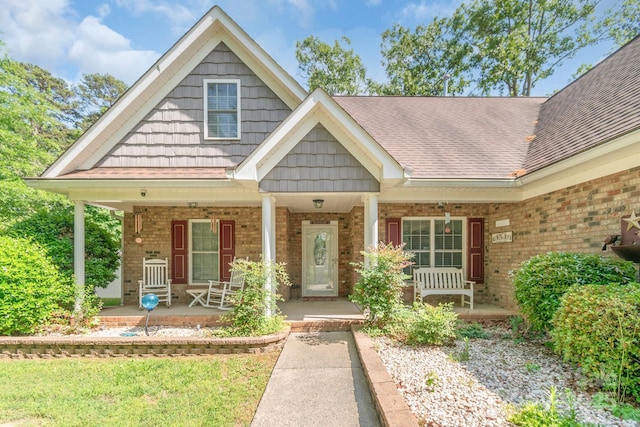 view of front of home featuring covered porch, brick siding, and a shingled roof