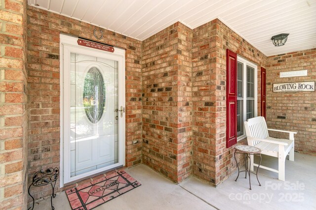 view of exterior entry featuring a porch and brick siding