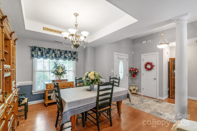 dining room with a chandelier, light wood-style floors, baseboards, a raised ceiling, and decorative columns