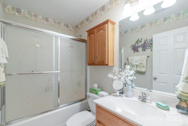 bathroom featuring toilet, combined bath / shower with glass door, and vanity