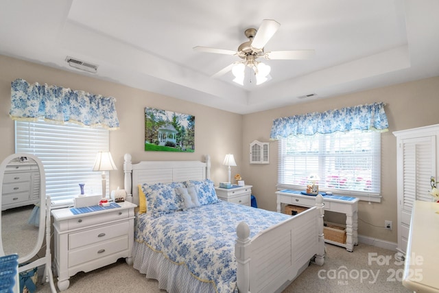 bedroom with a raised ceiling, light colored carpet, baseboards, and a ceiling fan
