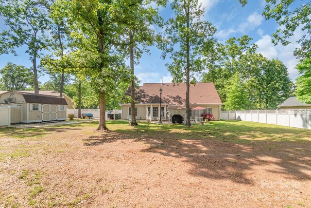 rear view of house with a storage shed, an outdoor structure, a fenced backyard, and a shingled roof