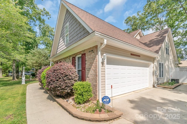view of side of property with brick siding, concrete driveway, an attached garage, a shingled roof, and a yard