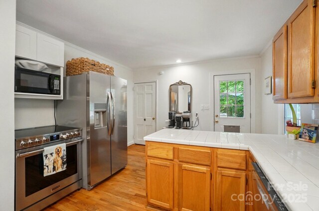 4647 General Pershing Dr, Charlotte, NC 28209 - kitchen with appliances with stainless steel finishes, a peninsula, light wood-style floors, tile countertops, and brown cabinets