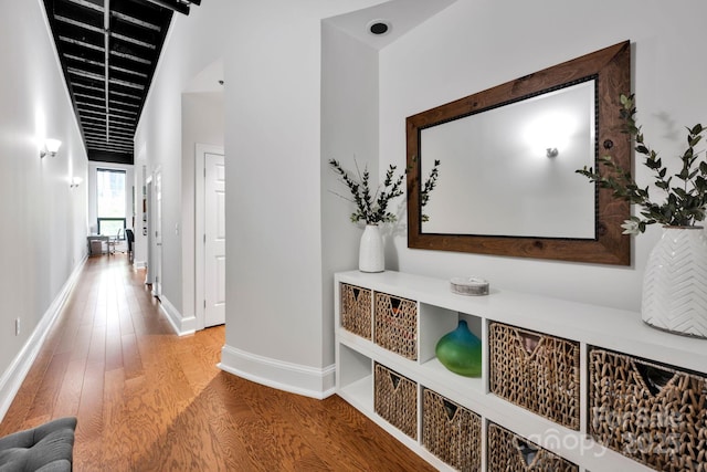 hall with wood finished floors, baseboards, and vaulted ceiling