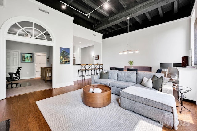 living area featuring a towering ceiling, wood finished floors, rail lighting, baseboards, and a chandelier