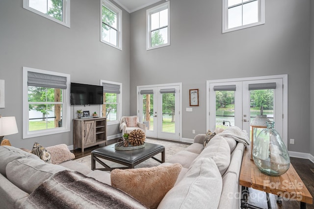 living room featuring french doors, a high ceiling, baseboards, wood finished floors, and crown molding