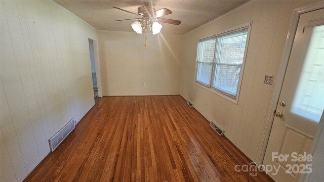 spare room featuring crown molding, wood finished floors, wooden walls, ceiling fan, and a textured ceiling